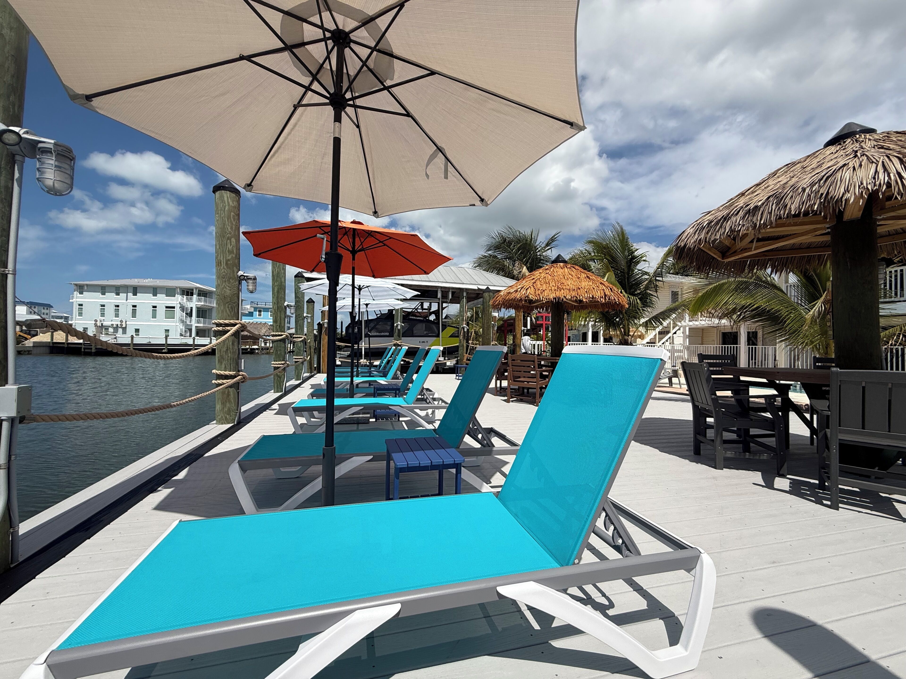 Une terrasse au bord de l’eau, dotée de chaises longues, de parasols et d’une structure à toit de chaume.