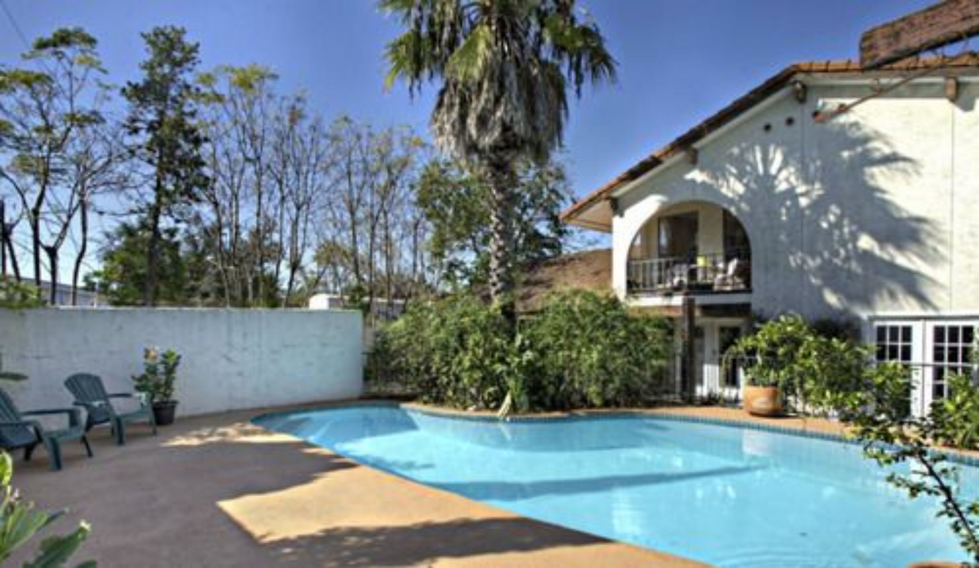 Una propiedad residencial con piscina, un porche cubierto y un edificio de dos plantas con balcón.