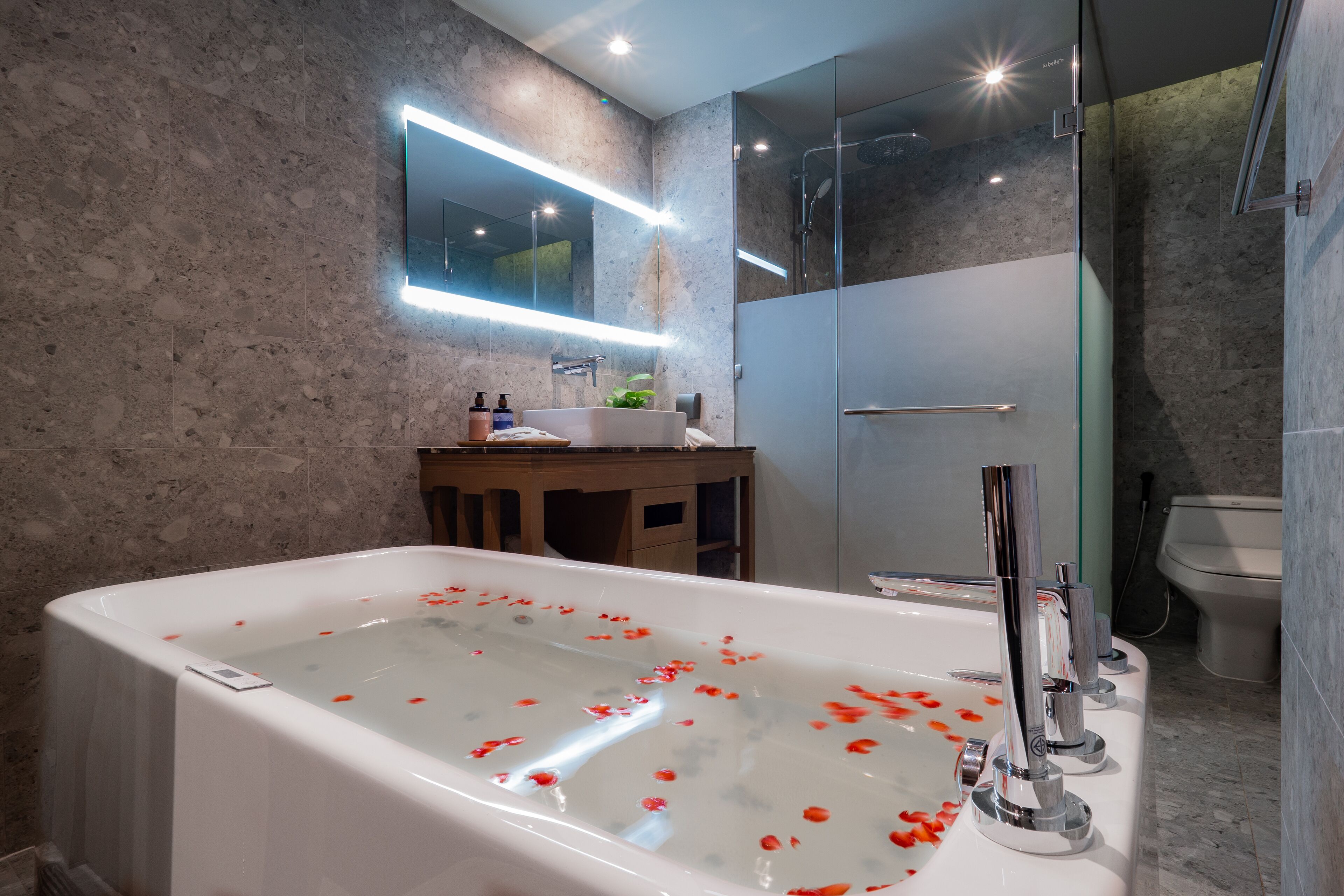 Un baño moderno con una bañera independiente, una ducha con cerramiento de vidrio y un revestimiento de mármol en la pared.