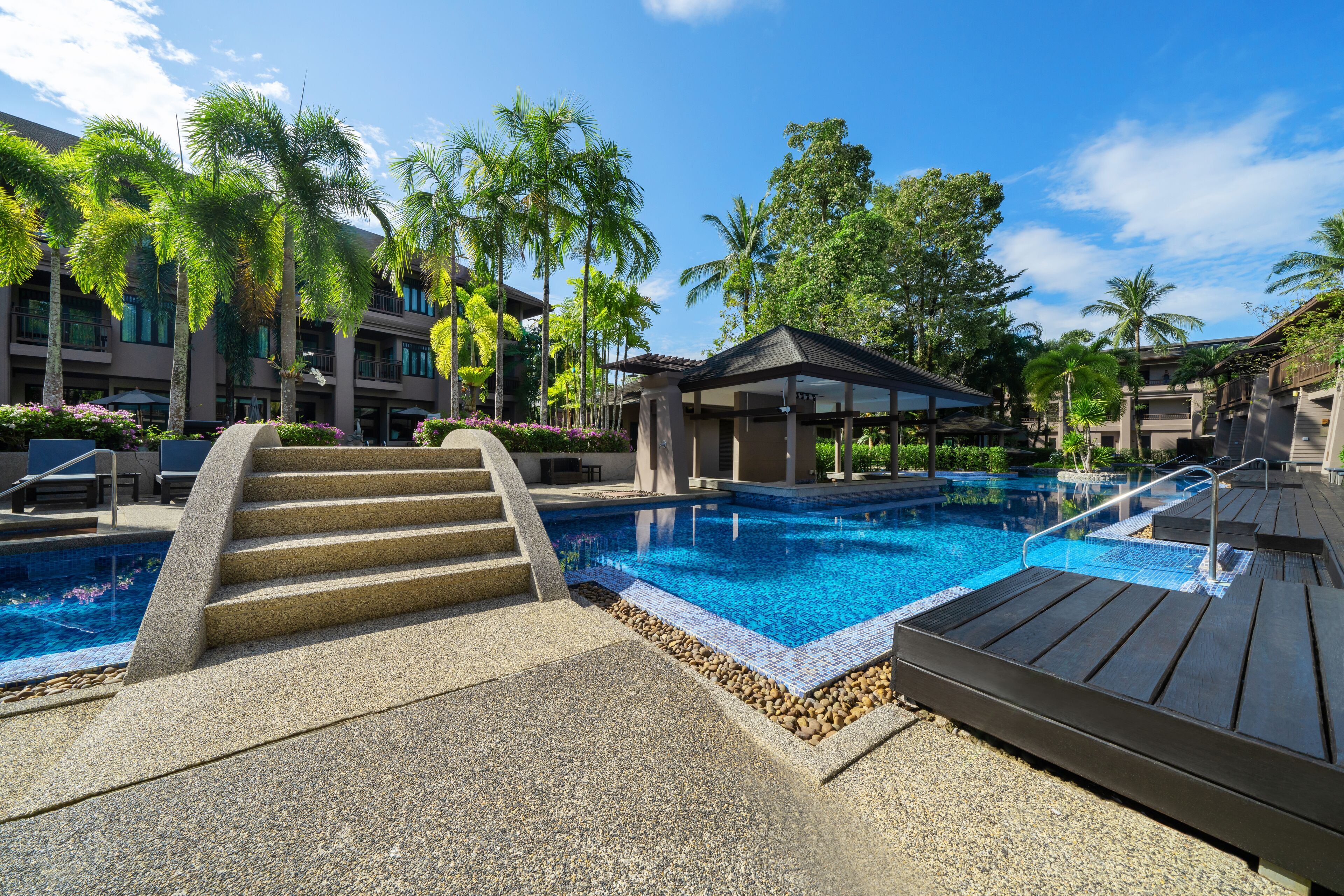 A pool area with steps leading into the water, surrounded by palm trees and a covered seating area.