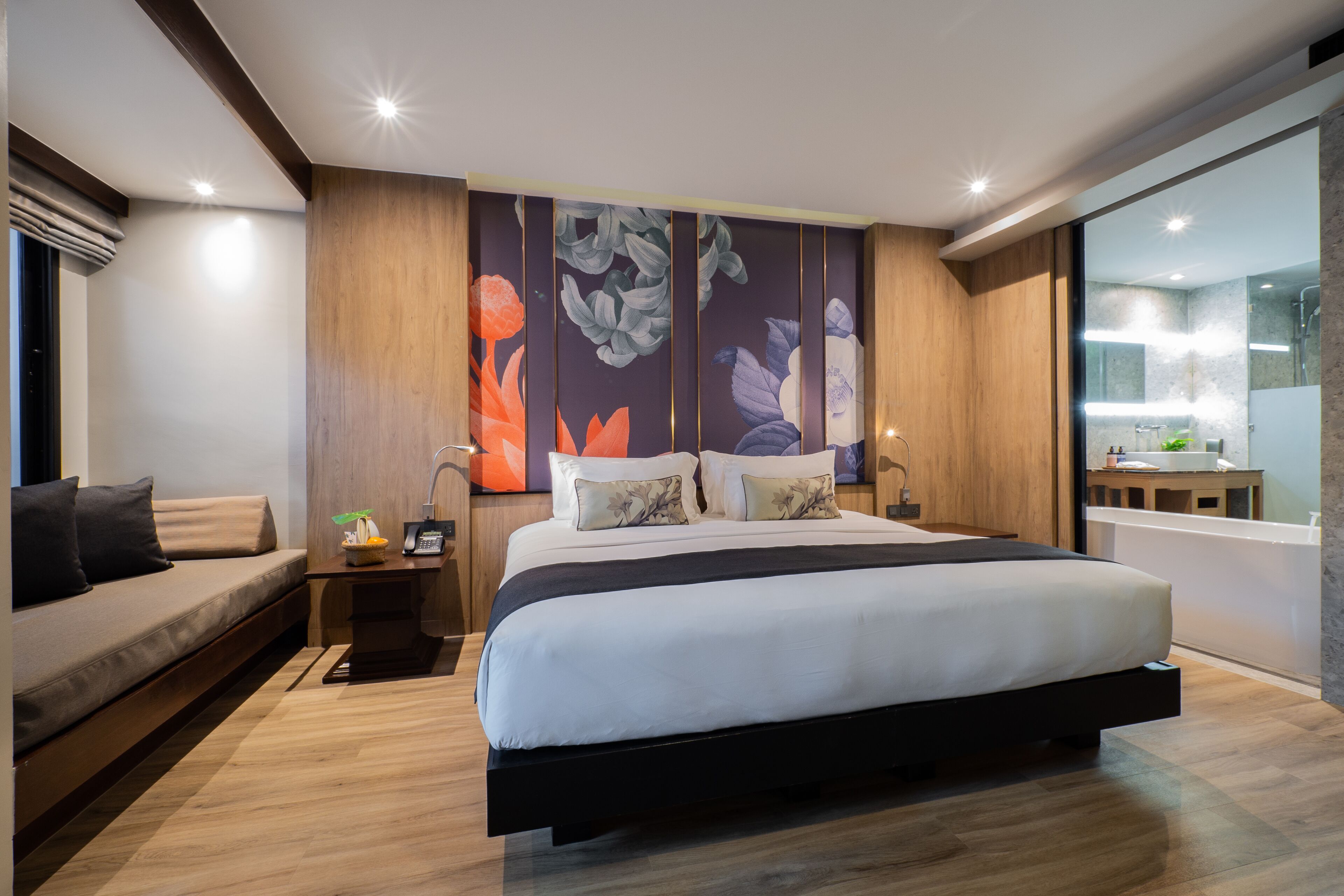 A modern bedroom with a large bed, a sofa, a nightstand, and a wall with a floral mural.