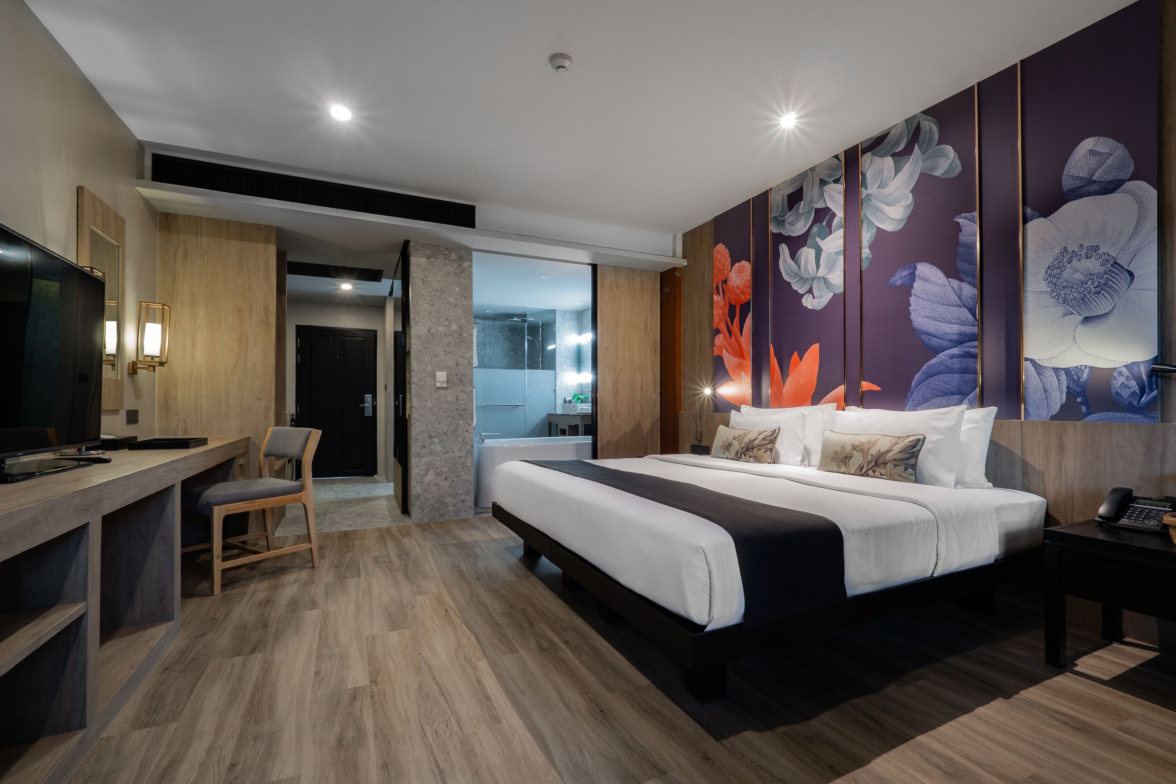 A modern hotel room with a large bed, a desk, and a chair. There is a bathroom visible through an open door.
