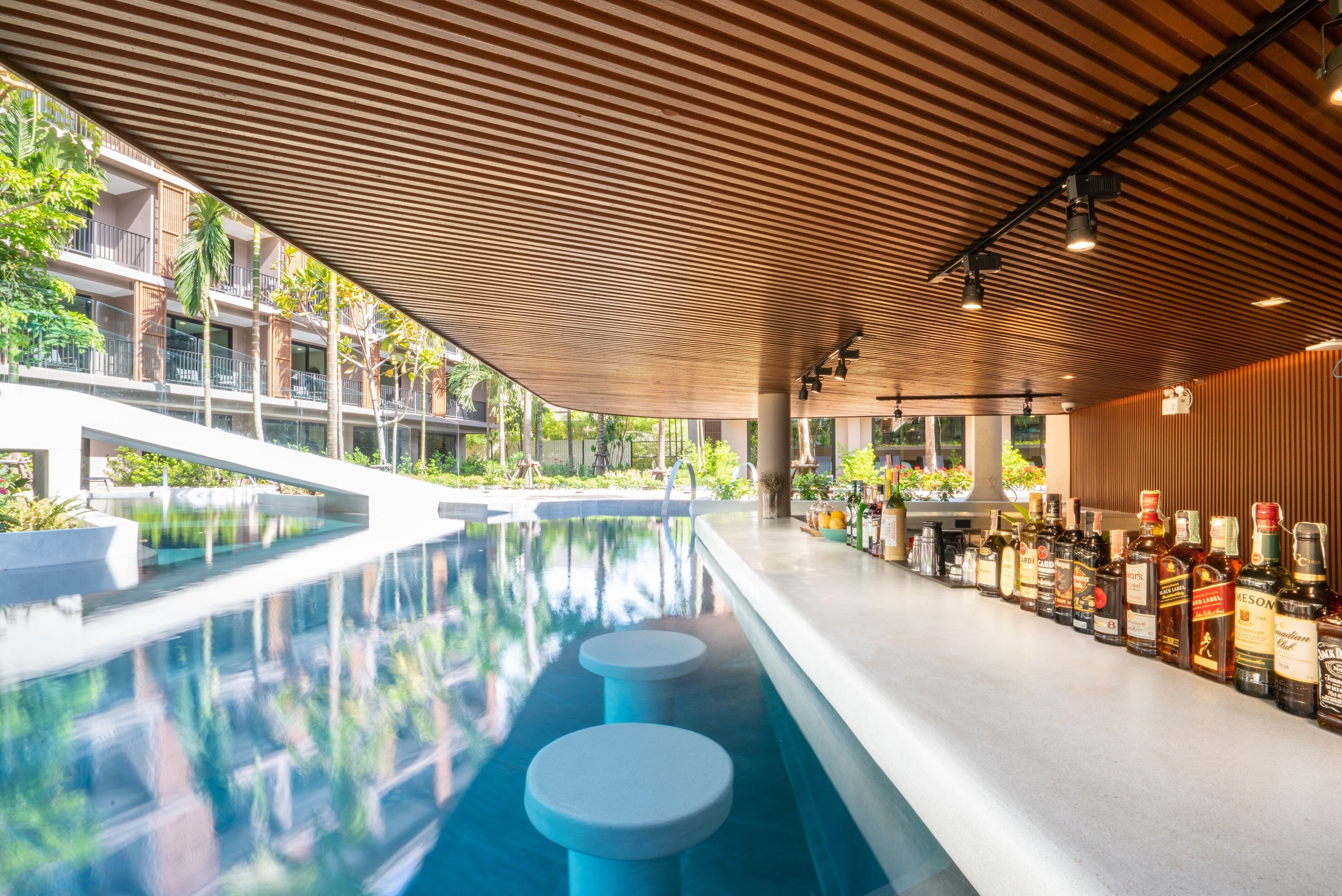 A modern indoor pool area with a wooden ceiling and a bar with various liquor bottles.