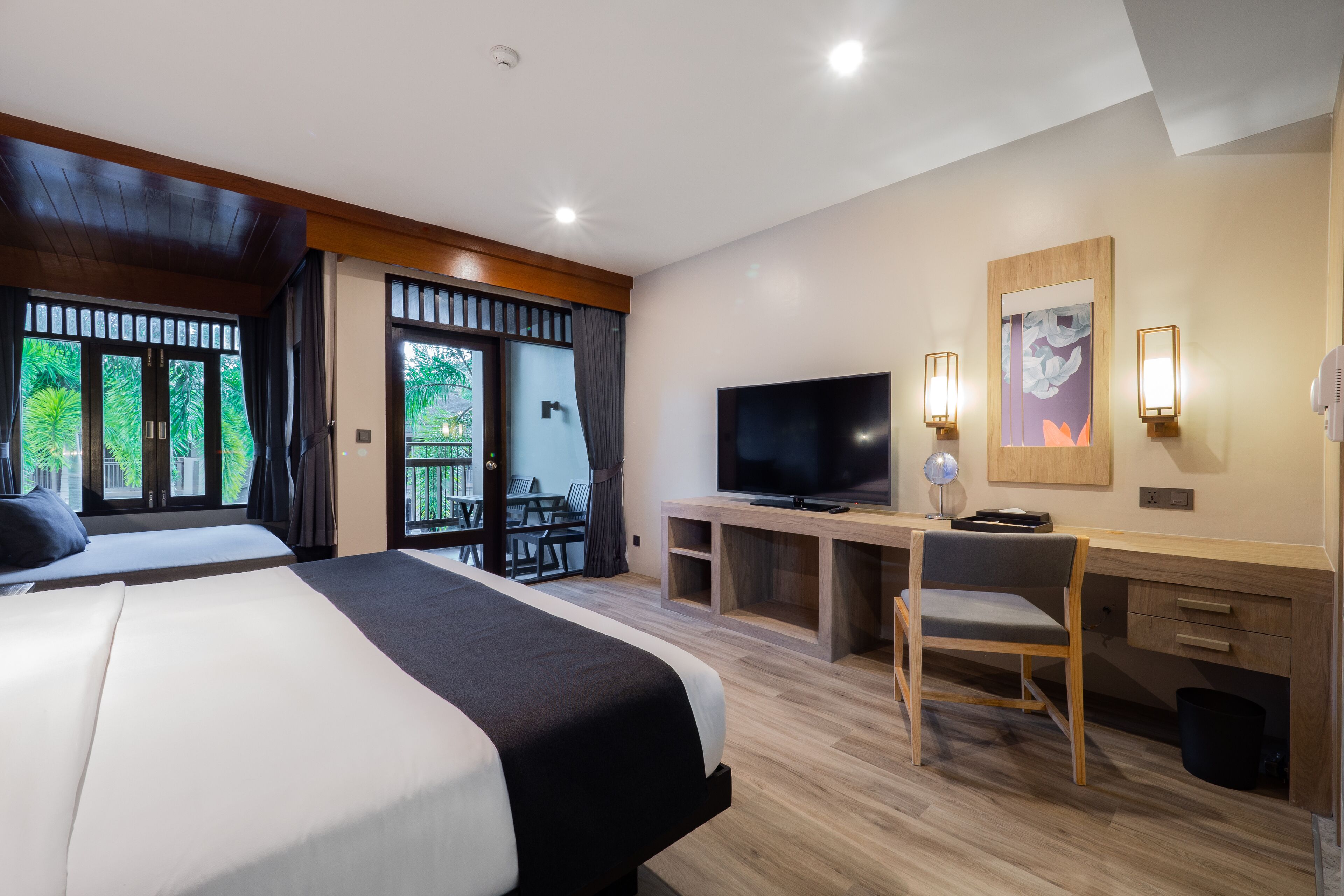 A hotel room with a large bed, a desk with a chair, a television, and a balcony with a table and chairs.