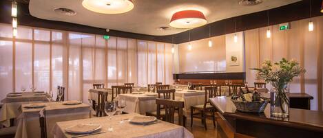 A restaurant with multiple tables, each set with wine glasses and plates, and a vase with flowers on the counter.