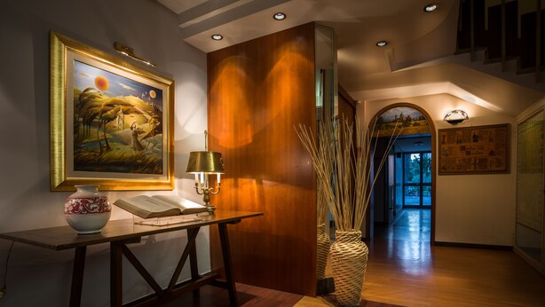 A reception area with a wooden reception desk, a framed painting, a vase, and a lamp. - Hotel Frate Sole (Assisi)