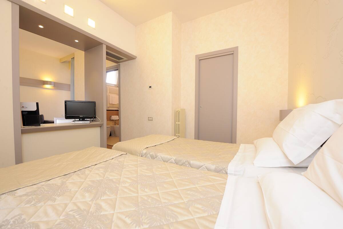 Una habitación de hotel con dos camas, un escritorio con una computadora y una puerta.