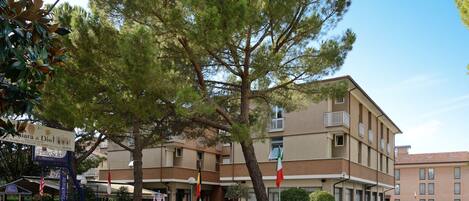 Un hotel con un patio central, palos de bandera y una zona de estacionamiento.