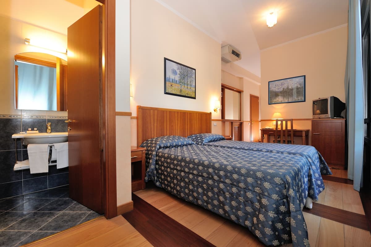 Una habitación de hotel con cama, baño con lavamanos y dos cuadros en las paredes.