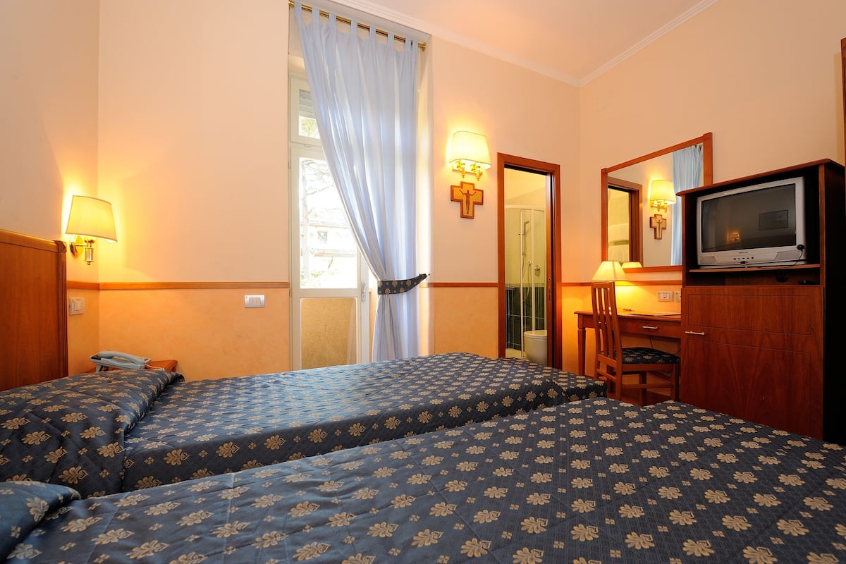 Una habitación de hotel con dos camas, un escritorio con silla, un televisor y un espejo.