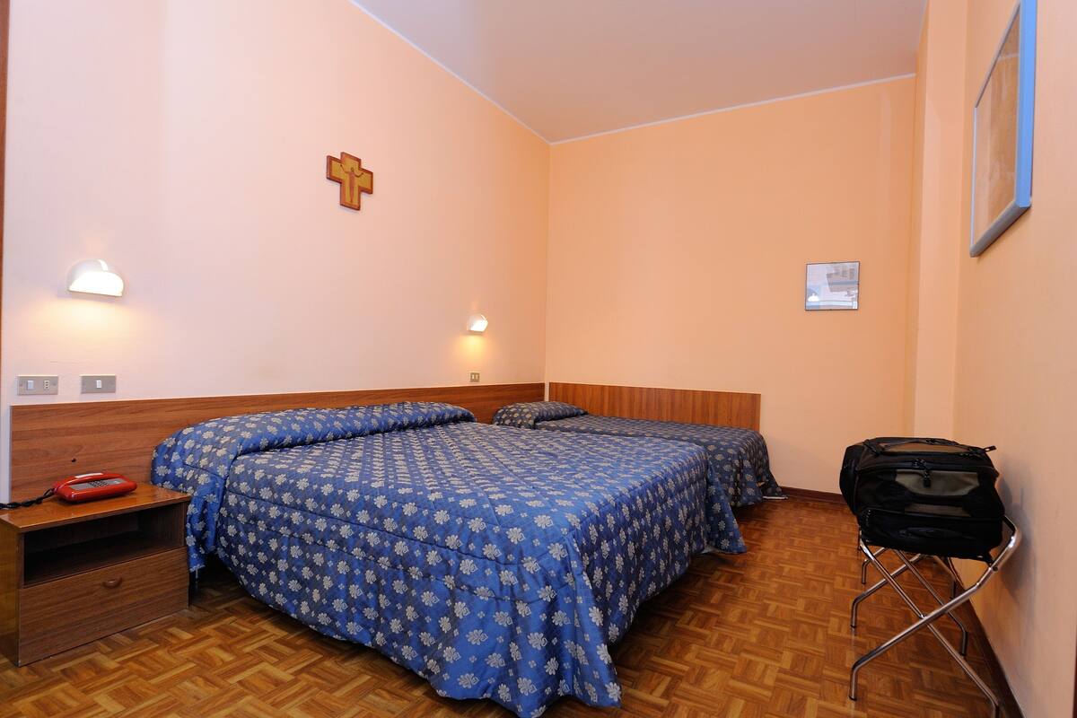Un dormitorio con dos camas, cabeceros de madera, mesitas de noche y una cruz colgada en la pared.