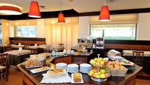 A breakfast buffet with various food items, including fruits, pastries, and beverages, in a well-lit dining area with tables and chairs. - Hotel Frate Sole (Assisi)