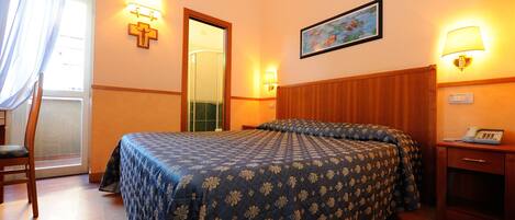 Quarto de hotel com cama, uma cadeira, escrivaninha com telefone e um quadro na parede.