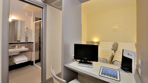A hotel room with a glass shower enclosure, a flat-screen TV, a bedside table with a remote control, and a bed with a headboard. - Hotel Frate Sole (Assisi)