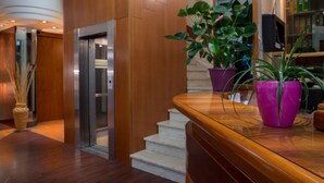 A reception area with a wooden reception desk, a potted plant, and a staircase leading to an elevator. - Hotel Frate Sole (Assisi)