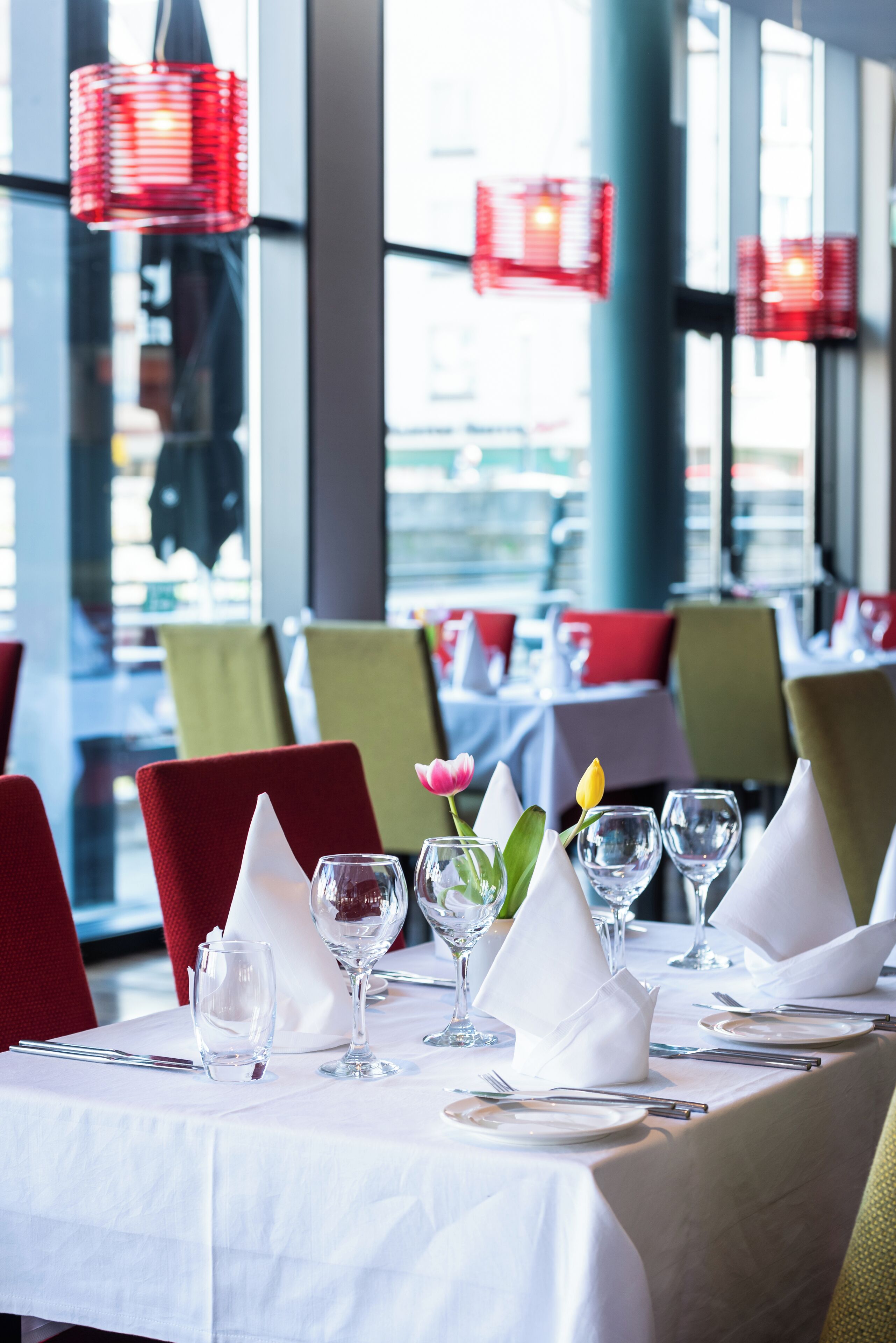 A restaurant table set with white tablecloths, red chairs, and a tulip centerpiece.