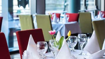 Uma mesa de restaurante posta com toalhas brancas, cadeiras vermelhas e um arranjo de tulipas.