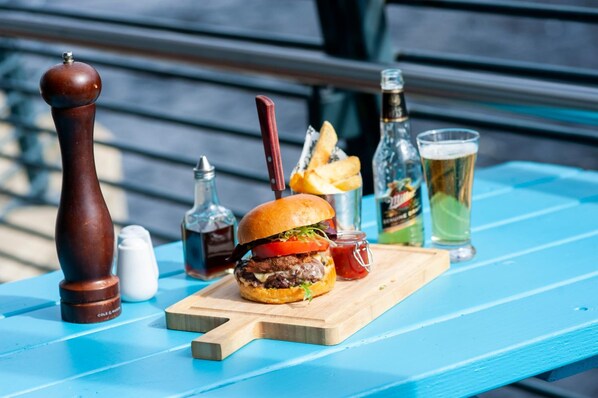 Una comida con una hamburguesa, papas fritas y una bebida sobre una mesa azul al aire libre.
