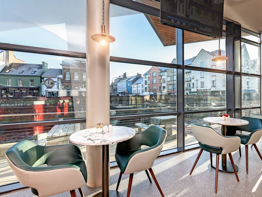 A modern interior with large windows, round tables, and green chairs.