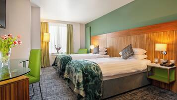 A hotel room with two beds, a green chair, a glass table with a vase of flowers, and a wooden headboard.
