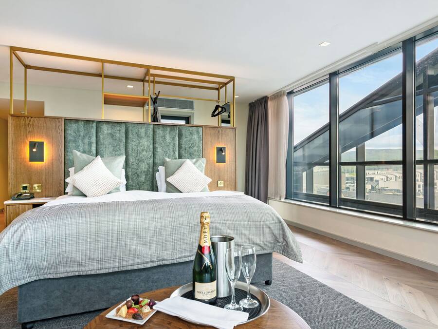 Habitació d'hotel moderna amb un llit gran, un minibar, una ampolla de xampany i vista a la ciutat.