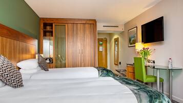 Habitación de hotel con cama, escritorio con silla, televisión montada en la pared y espejo.