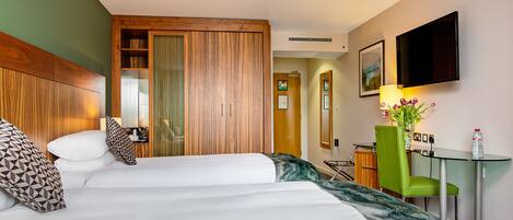 A hotel room with a bed, a desk with a chair, a TV mounted on the wall, and a mirror.
