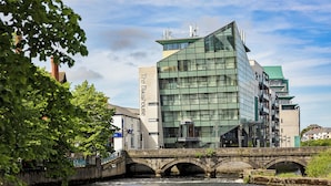 A modern building with a glass facade and a bridge over a river.