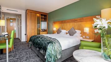 Habitación de hotel con cama, escritorio, silla, una mesita y un florero con flores.