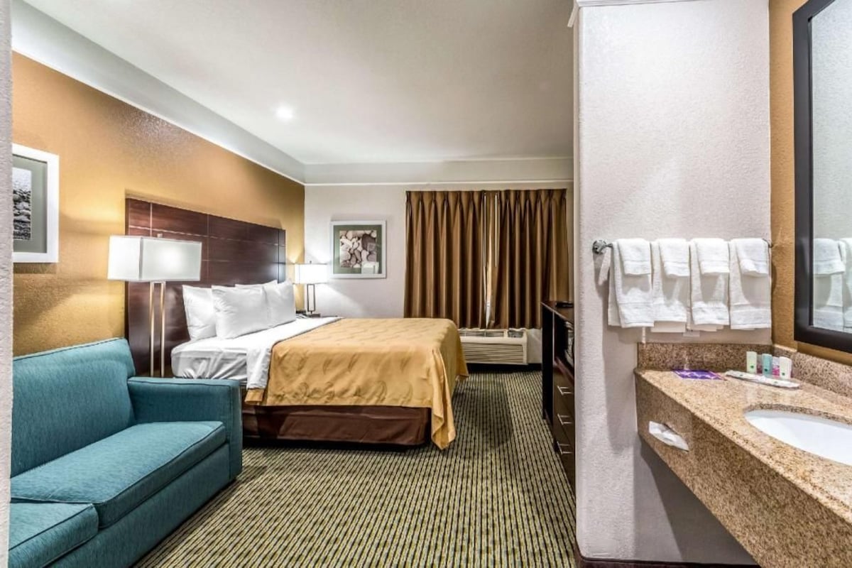 A hotel room with a bed, a sofa, a bathroom with a sink and mirror, and a curtain.