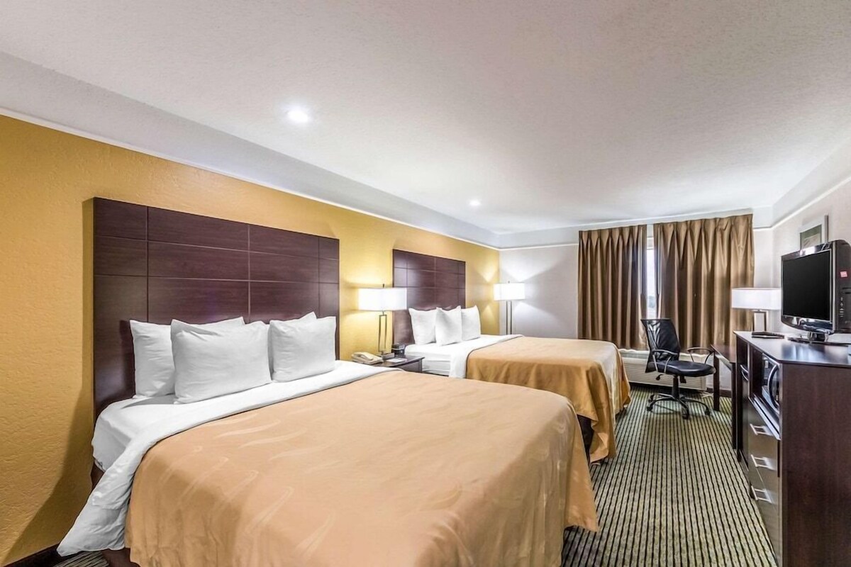 A hotel room with two beds, a desk with a television, and a window with curtains.