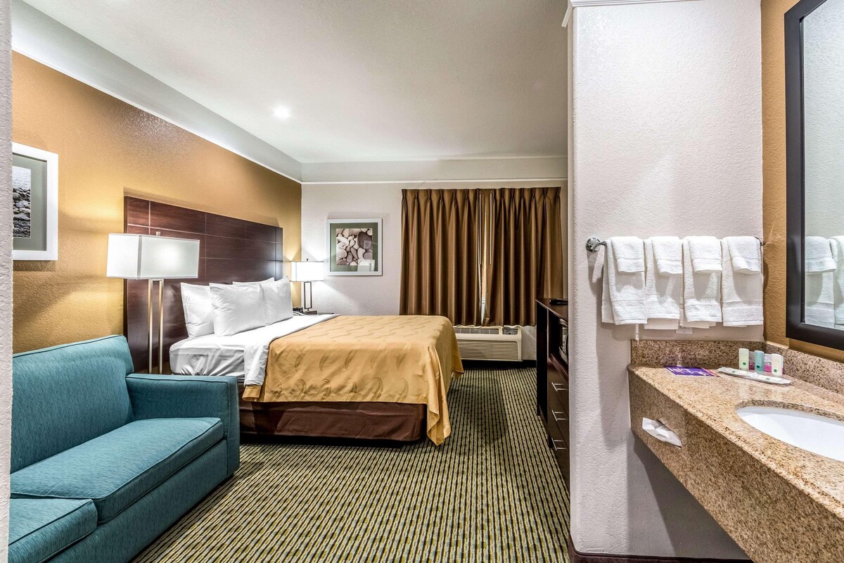 A hotel room with a bed, a sofa, a bathroom with a sink and towels, and a large mirror.