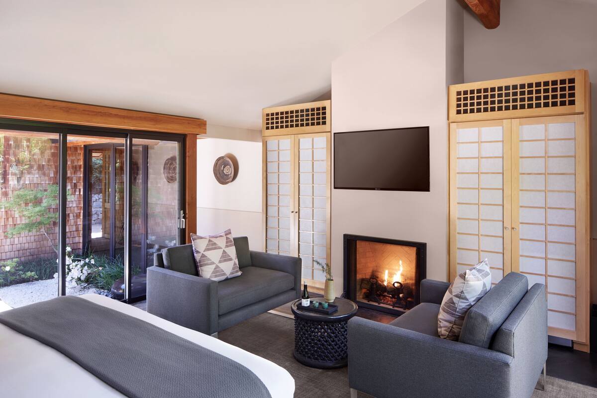 A modern bedroom with a bed, two sofas, a fireplace, and a TV.