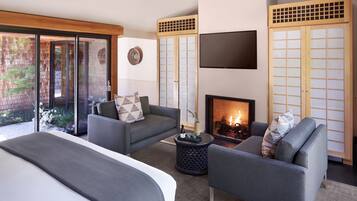 A modern bedroom with a bed, two sofas, a fireplace, and a TV.