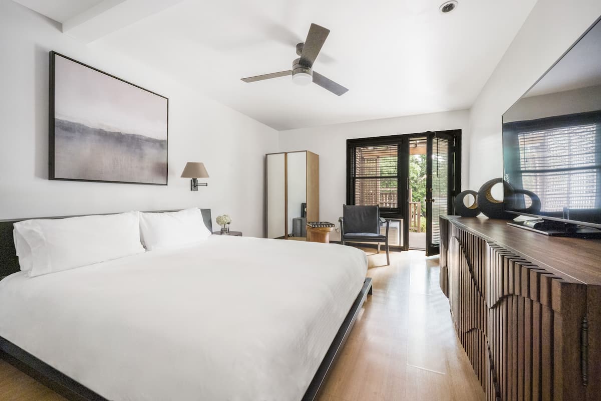 A modern hotel room with a large bed, a ceiling fan, a TV, and a view of the outdoors.