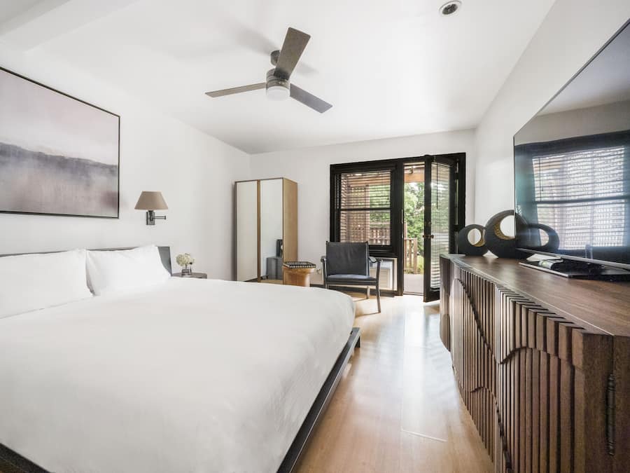 A modern hotel room with a large bed, a ceiling fan, a TV, and a view of the outdoors.