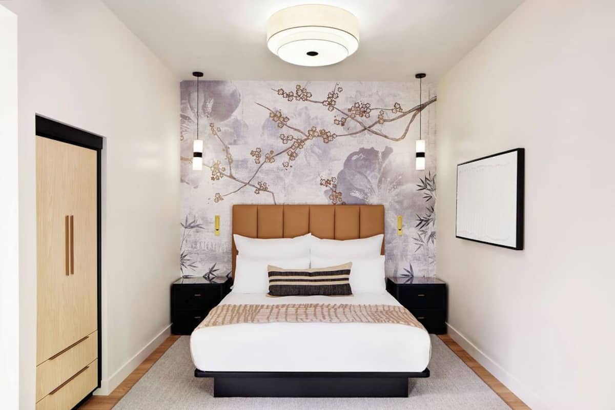 A bedroom with a bed, nightstands, a wardrobe, and a wall with a floral pattern.