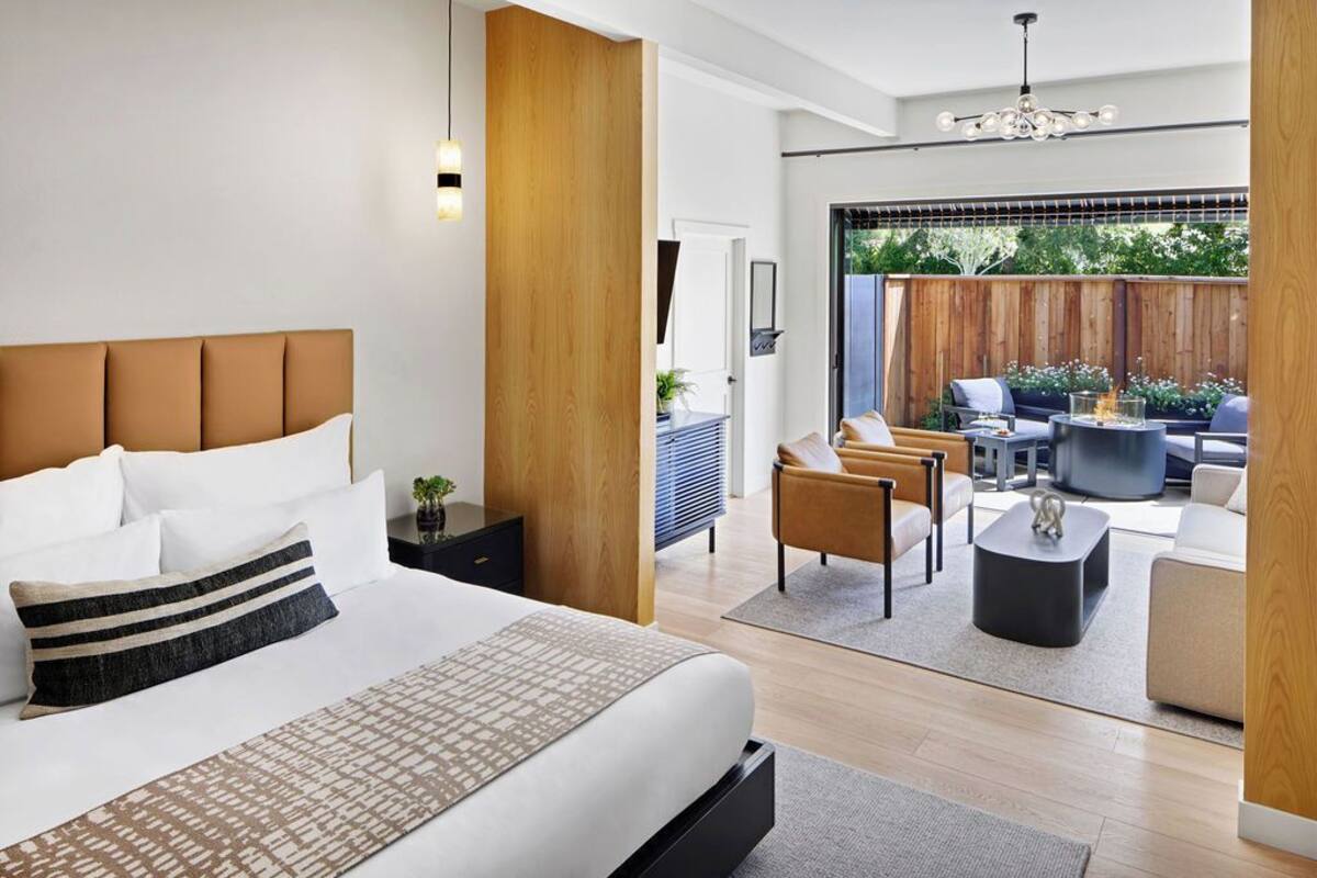 A modern bedroom with a large bed, a wooden accent wall, and a view of an outdoor patio area with seating.