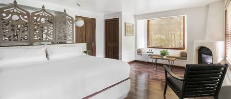 A spacious bedroom with a large bed, a wooden floor, a seating area with a bench and a small table, and a fireplace.