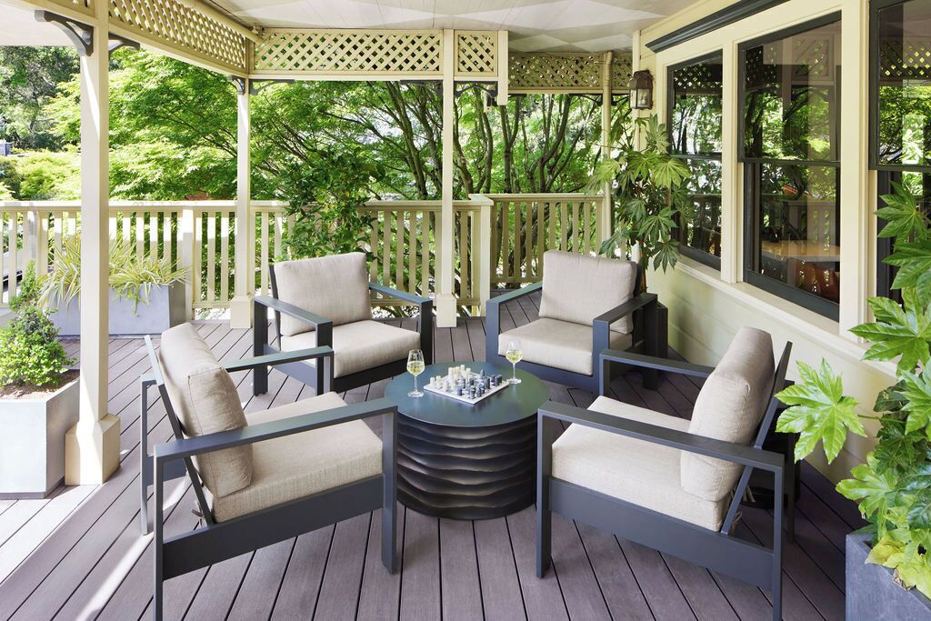 A covered outdoor seating area with four chairs and a round table, surrounded by wooden railings and potted plants.