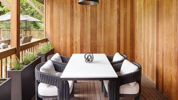 A covered patio area with a white table and wicker chairs, surrounded by wooden panel walls and a wooden deck.