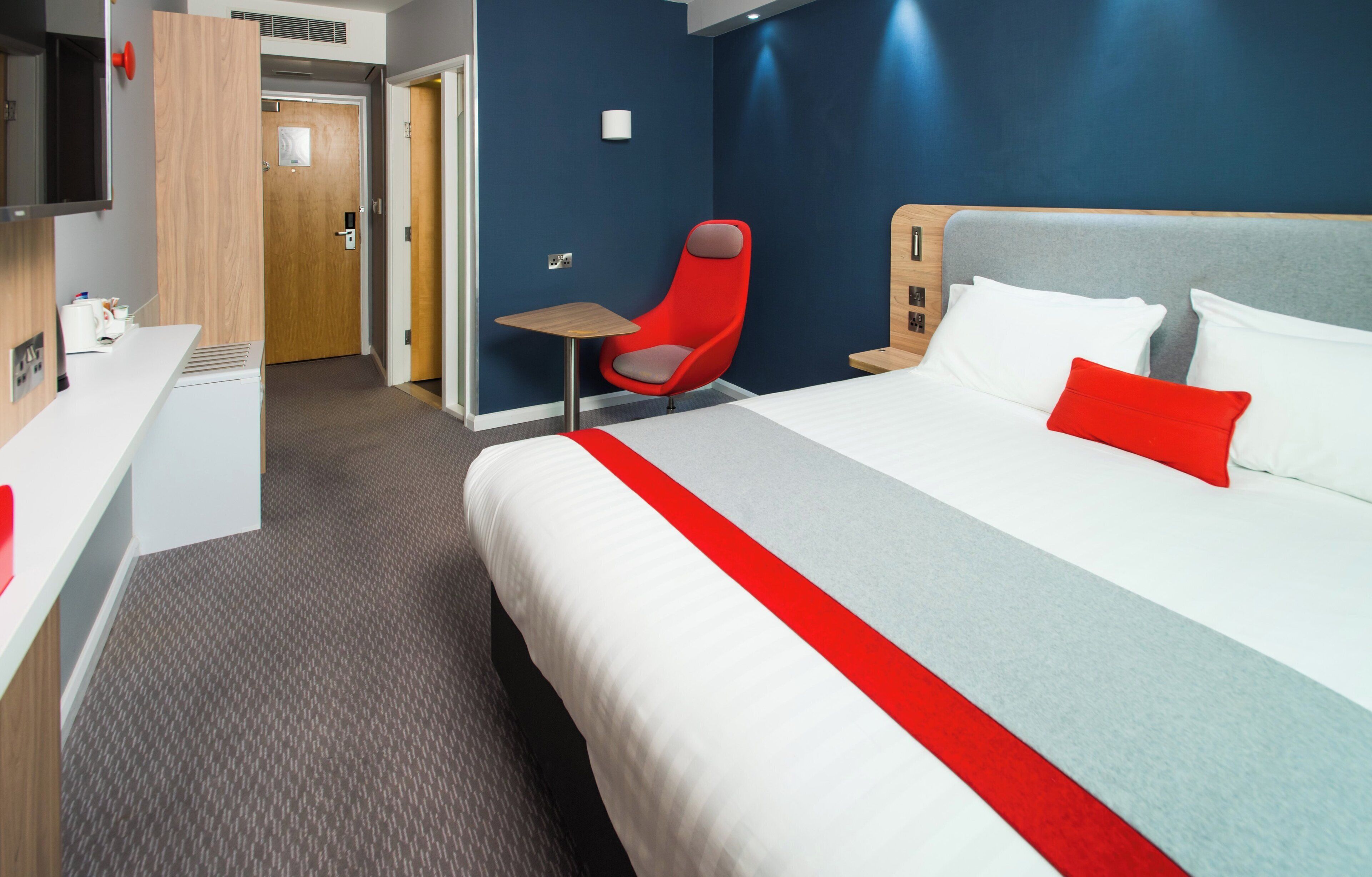 A hotel room with a bed, a desk, a chair, and a TV.