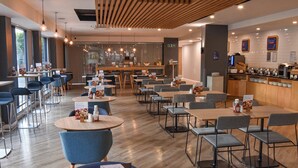 A modern restaurant with round tables and blue chairs, a bar area, and a view through a glass wall. - Holiday Inn Express Leeds City Centre Armouries by IHG (Leeds)