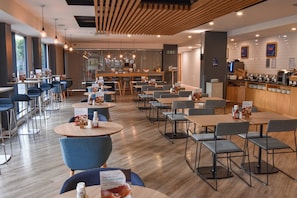 A modern restaurant with round tables and blue chairs, a bar area, and a view through a glass wall. - Holiday Inn Express Leeds City Centre Armouries by IHG (Leeds)