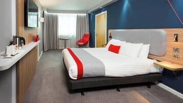 A hotel room with a bed, a desk, a chair, a television, and a window with curtains.