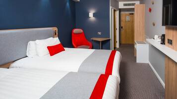 Une chambre d’hôtel avec deux lits, un fauteuil rouge, une petite table, un téléviseur et un coin cuisine.