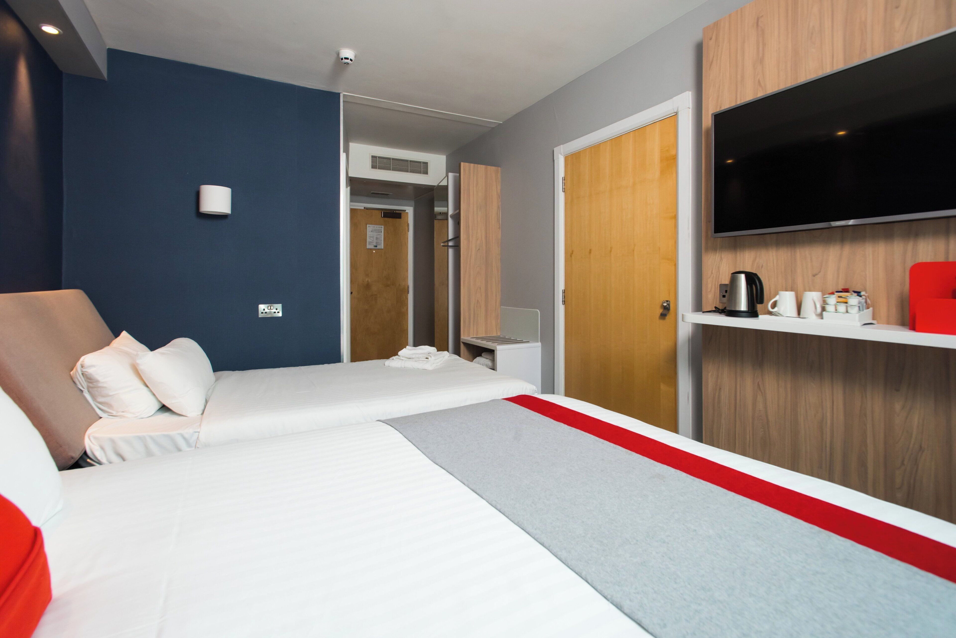 A hotel room with a bed, a television, a coffee maker, and a red chair.