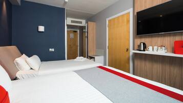 A hotel room with a bed, a television, a coffee maker, and a red chair.
