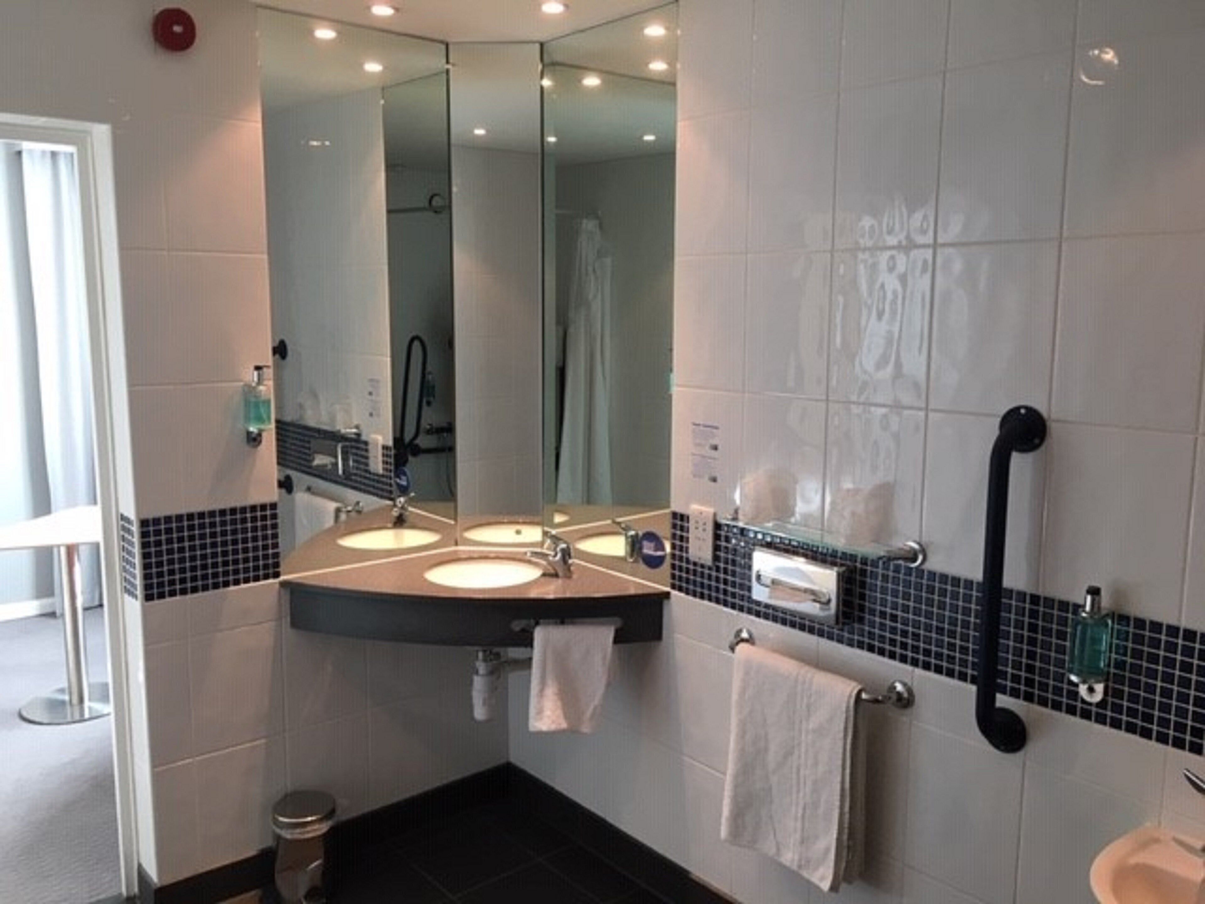 A bathroom with two sinks, a large mirror, a black grab bar, and a towel rack.