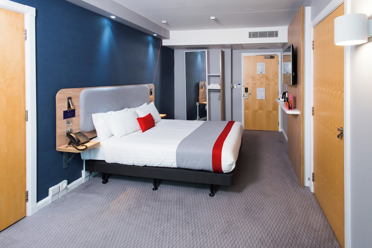A hotel room with a bed, bedside table, phone, and a mirror.